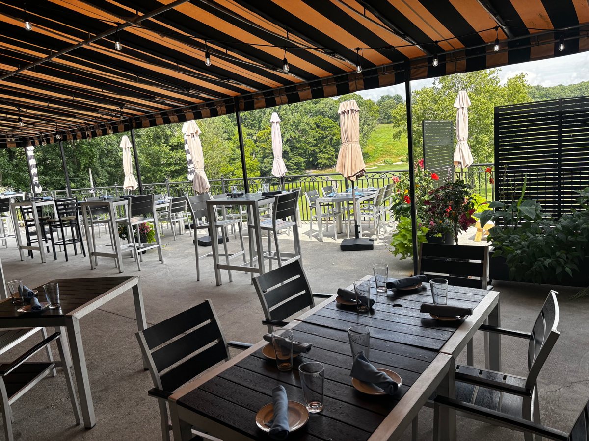 Tables under the striped awning on the patio deck, looking out over the golf course