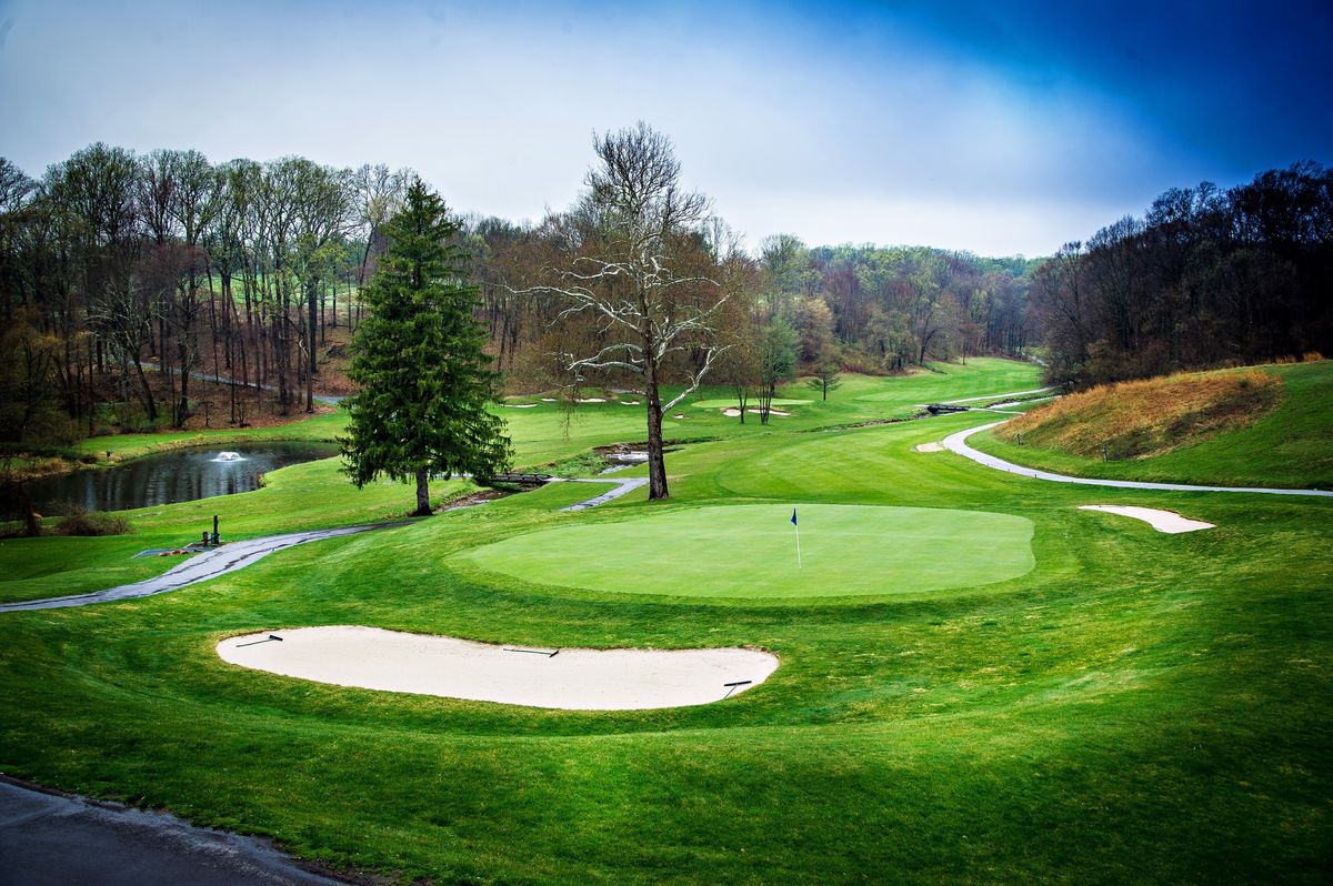 A green and bunker on the Paxon Hollow golf course, with a pond and tree-lined fairway beyond