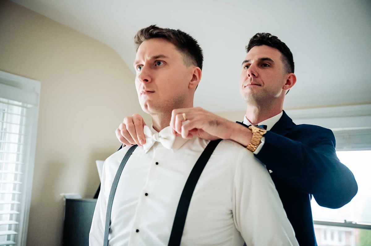 Groomsman helping the groom with his suspenders
